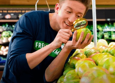 Fresh Thyme employee inspecting a mango with a magnifying glass